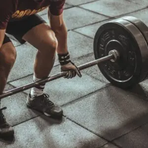 A focused weightlifter prepares to lift a heavy barbell in an indoor gym setting.